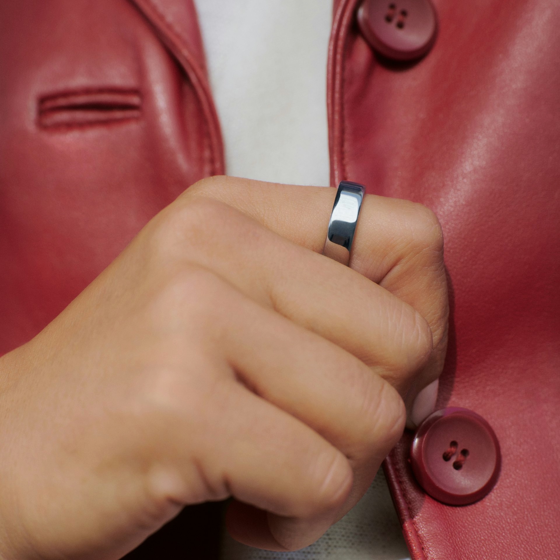 Close view of a silver smart ring on a hand against a red leather jacket